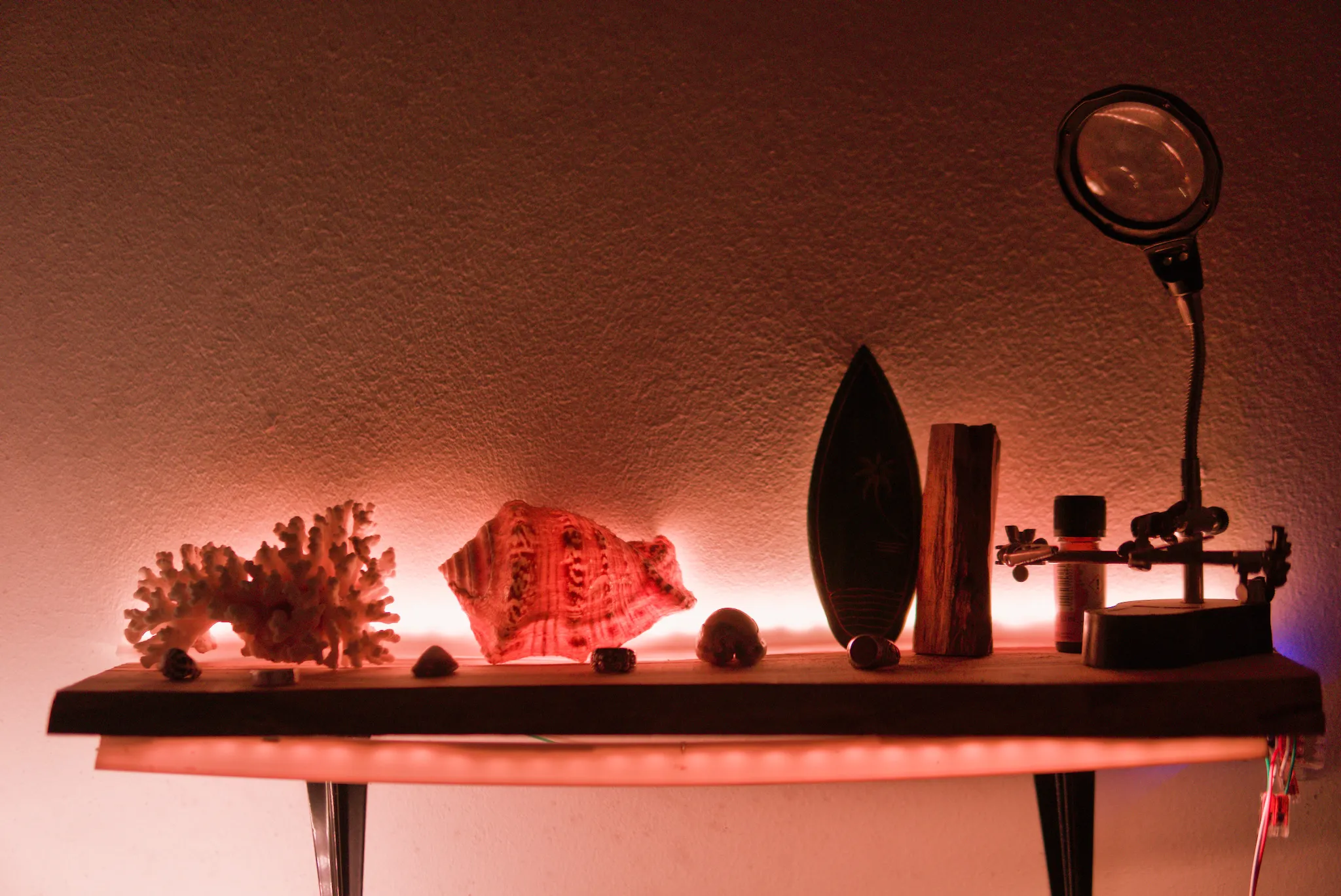 Wall shelf lit by warm addressable LED lighting, with decorative objects and a magnifying lamp.